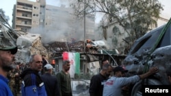People gather near a damaged site, hauling a destroyed vehicle away, after what Syrian and Iranian media described as an Israeli airstrike on Iran's consulate in the Syrian capital Damascus, April 1, 2024.
