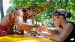 Txatxu Pataxo, left, of the Pataxo people of Bahia, Brazil, shows Eva Quiroz, 16, of Takoma Park, Maryland, how to draw a pattern traditional used in body painting, during the Smithsonian Folklife Festival in Washington, June 26, 2024.