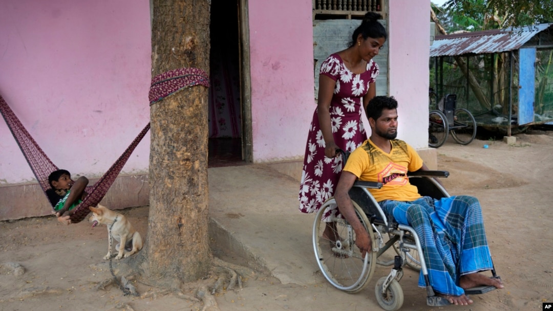 FILE - Thangarasa Kirubakaran, a former rebel fighter who was disabled in the civil war, gets help from his wife as he sits in a wheelchair outside his home in Mullaitivu, Sri Lanka, May 6, 2023. 