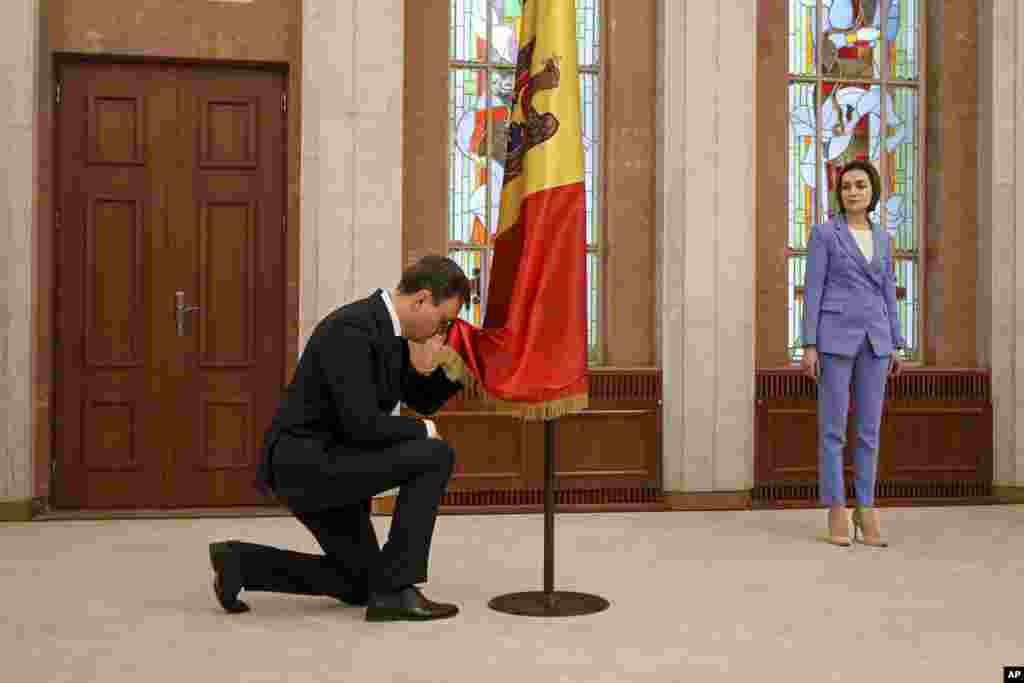Moldova&#39;s president Maia Sandu, right, watches as Prime Minister Dorin Recean kneels down in front of the national flag during a swearing-in ceremony in Chisinau.