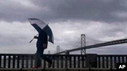 Un peatón lleva un paraguas mientras camina frente al puente de la bahía de San Francisco-Oakland en San Francisco, el martes 21 de marzo de 2023. (Foto AP/Jeff Chiu)