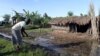 FILE - Fiona Nakacwa clears water from her compound in the Lwera wetlands near Lukaya, Uganda on April 5, 2023. 