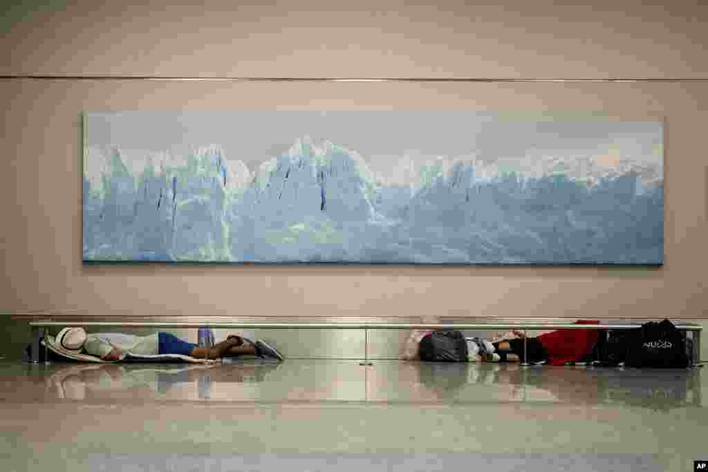 Homeless men sleep below a photo of the Perito Moreno Glacier at the Jorge Newbery international airport, commonly known as Aeroparque, in Buenos Aires, Argentina. More than 100 homeless people sleep every night in a common area of the Aeroparque.
