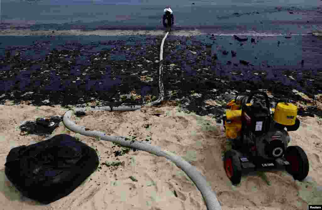 A worker operates a vacuum system during a cleanup of an oil slick at Tanjong Beach in Sentosa, Singapore.
