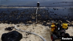 A worker operates a vacuum system during a cleanup of an oil slick at Tanjong Beach in Sentosa, Singapore.