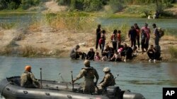 Penjaga mendorong para migran yang menunggu di gundukan pasir di tengah sungai Rio Grande untuk berbalik ketika mereka mencoba menyeberangi sungai tersebut dari Meksiko ke AS, Sabtu, 23 September 2023. (AP/Eric Gay)