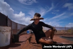 Tina Taniguchi prepares one of her family's many salt beds by rubbing it with a smooth river rock on July 10, 2023, in Hanapepe, Hawaii. (AP Photo/Jessie Wardarski)