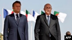 FILE— French President Emmanuel Macron (L) stands next to Algeria's President Abdelmadjid Tebboune (R) at Algiers airport, in Algiers, on August 27, 2022.