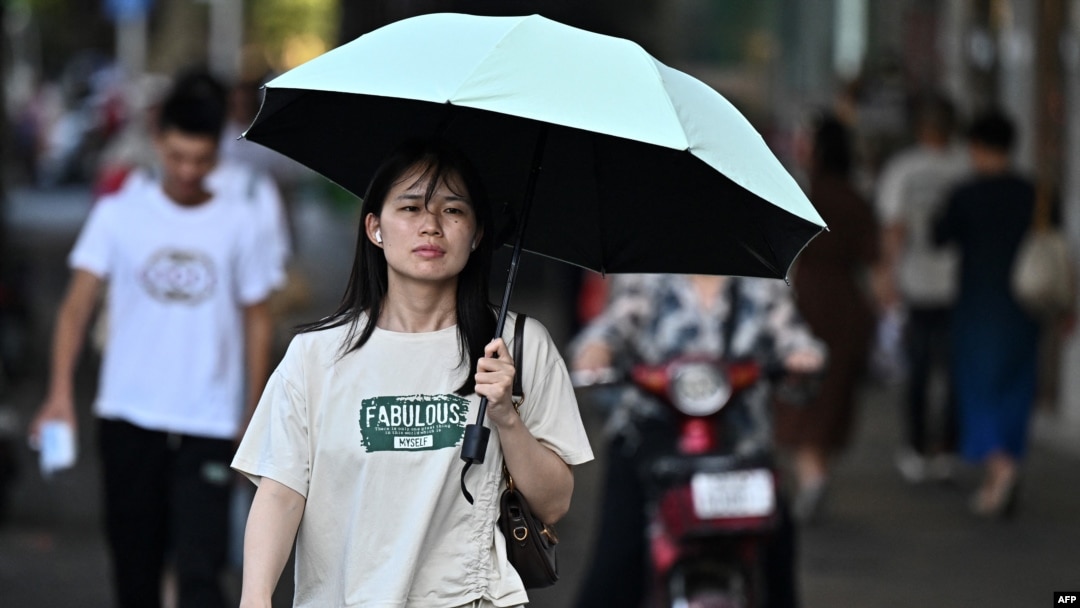 Seorang perempuan berjalan di tengah cuaca terik di Provinsi Hubei, 1 Agustus 2024. (Foto: Pedro Pardo/AFP)
