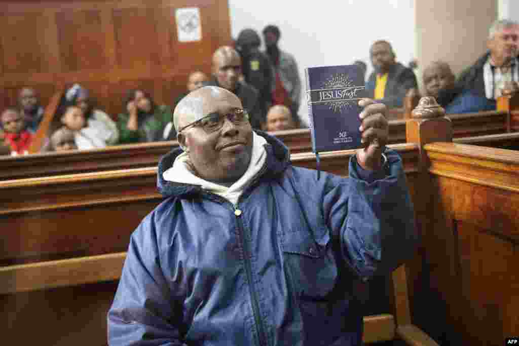 Fulgence Kayishema, one of the last fugitives sought for their role in the 1994 Rwanda genocide, holds up a Christian book as he sits in the Cape Town Magistrate's Court in Cape Town, two days after being arrested following 22 years on the run.