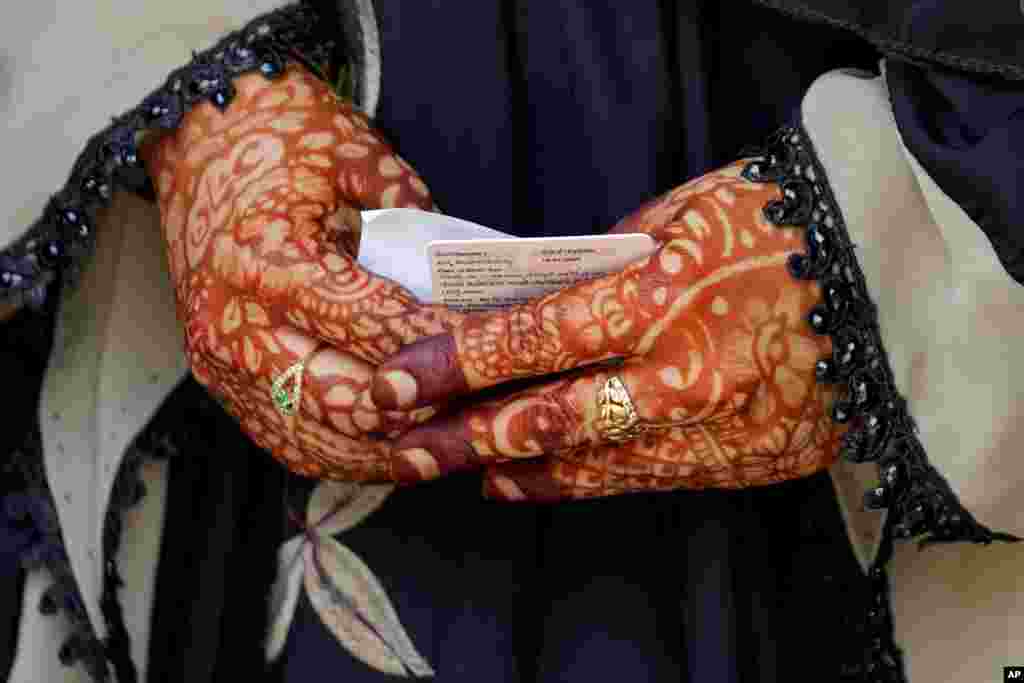 A woman whose hands are decorated with henna holds her voter identity card while waiting to cast her vote at a polling station in Bengaluru, India.