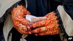 A woman whose hands are decorated with henna holds her voter identity card while waiting to cast her vote at a polling station in Bengaluru, India.