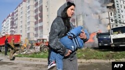 A woman walks past damaged residential buildings as she carries a child in Uman, April 28, 2023, after Russian missile strikes targeted several Ukrainian cities. 