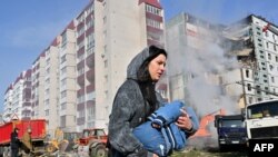 A woman walks past damaged residential buildings as she carries a child in Uman, around 215 km south of Kyiv, on April 28, 2023, after Russian missile strikes targeted several Ukrainian cities overnight. (Photo by Sergei SUPINSKY/ AFP)