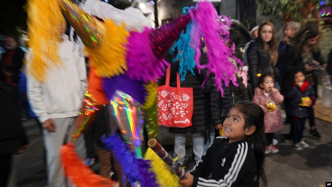 A child swings at a pinata during a street "posada" organized by neighbors in Mexico City, Dec. 22, 2023. 