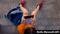 FILE - A boy plays with his father's phone outside school in Barcelona, Spain, on June 17, 2024. (AP Photo/Emilio Morenatti)
