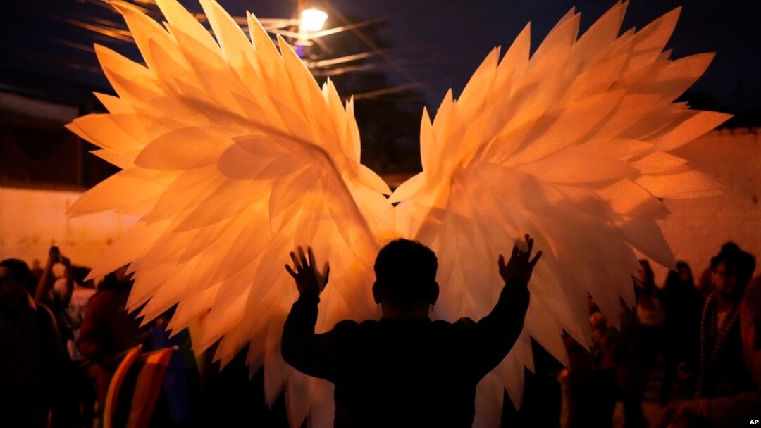 A reveler is silhouetted against a pair of angel wings as they help a performer with a costume during a Gay Pride parade marking the culmination of LGBTQ+ Pride month, in Asuncion, Paraguay, June 29, 2024. 