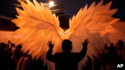 A reveler is silhouetted against a pair of angel wings as they help a performer with a costume during a Gay Pride parade marking the culmination of LGBTQ+ Pride month, in Asuncion, Paraguay, June 29, 2024. 