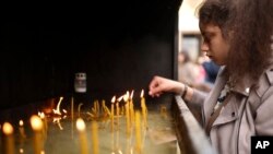 A woman lights candles in front of the St. Sava Serbian Orthodox temple in Belgrade, Serbia, May 4, 2023. 