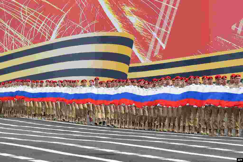 Gerakan Pemuda Patriotik Rusia Anggota Yunarmiya memegang bendera nasional raksasa di Lapangan Dvortsovaya (Istana) selama latihan umum untuk parade Hari Kemenangan di kota Saint Petersburg. (AFP)&nbsp;