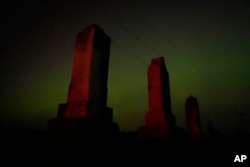 Old tombstones stand against the northern lights at a cemetery early Saturday, May 11, 2024, near Skidmore, Mo. (AP Photo/Charlie Riedel)