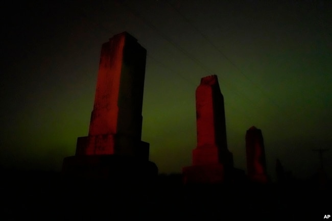 Old tombstones stand against the northern lights at a cemetery early Saturday, May 11, 2024, near Skidmore, Mo. (AP Photo/Charlie Riedel)