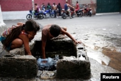 Children fill plastic containers with water at a street fountain in Petare, Venezuela.