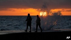 FILE - The sun rises above the Atlantic Ocean as waves crash near beachgoers on a jetty, Dec. 7, 2022, in Bal Harbour, Fla. Ocean temperatures have spiked well above record levels in recent weeks, and scientists are trying to determine what it means.