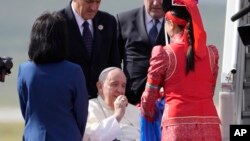 Paus Fransiskus mengambil sepotong keju Aaruul atau dadih Mongolia setibanya di bandara Internasional Ulaanbaatar Chinggis Khaan, Jumat, 1 September 2023. (AP/Andrew Medichini)