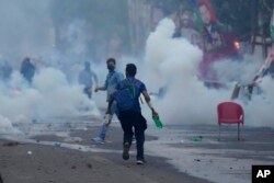 FILE - Supporters of former Prime Minister Imran Khan run for cover after police fire tear gas shells to disperse them during clashes outside Khan's residence, in Lahore, Pakistan, March 14, 2023.