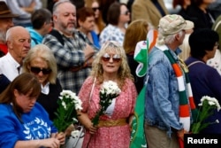 A woman holds flowers as fans gather outside late Irish singer Sinead O'Connor's former home to say their last goodbye to her on the day of her funeral procession, in Bray, Ireland, Aug. 8, 2023.