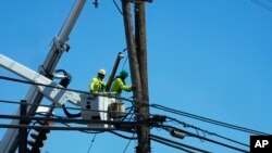 FILE - Linemen work on poles Aug. 13, 2023, in Lahaina, Hawaii, following a deadly wildfire that caused heavy damage days earlier.