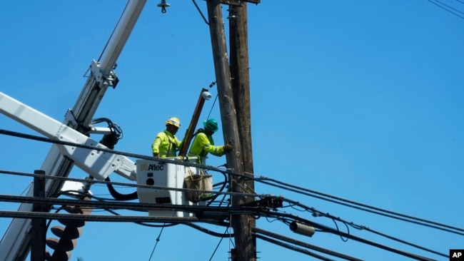 FILE - Linemen work on poles Aug. 13, 2023, in Lahaina, Hawaii, following a deadly wildfire that caused heavy damage days earlier.