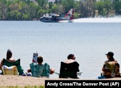 Beachgoers watch a 263 AeroFlite Scooper aircraft skim water off Chatfield Reservoir to then drop over the nearby Quarry Fire southwest of Littleton, Colorado, Aug. 1, 2024. (Andy Cross/The Denver Post via AP)