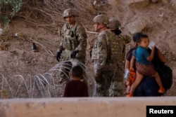 Migrants stand near the Rio Bravo river after crossing the border, to request asylum in the United States, as members of the Texas Army National Guard extended razor wire, as seen from Ciudad Juarez, Mexico, May 13, 2023.
