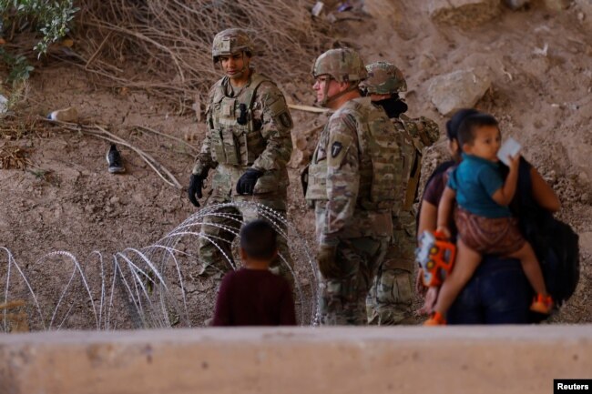 Migrants stand near the Rio Bravo river after crossing the border, to request asylum in the United States, as members of the Texas Army National Guard extended razor wire, as seen from Ciudad Juarez, Mexico, May 13, 2023.