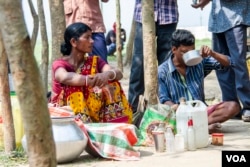 A tribal woman in eastern India sells Hadiya, an indigenous alcoholic drink, while a tribal man sits next to her drinking on March 30, 2024. (Ajharul Pathan/VOA)
