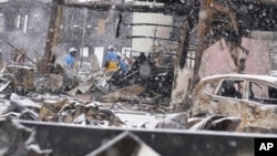 Snow falls as police officers continue a search operation around a burnt market in Wajima, Ishikawa prefecture, Japan, Jan. 7, 2024.