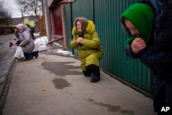 Mourners kneel as they await the coffin of Oleksandr Maksymenko, 38, to pass by during his funeral in his home-village Kniazhychi, east of Kyiv, Ukraine, Feb. 13, 2023. Oleksandr, a civilian who was a volunteer in the armed forces of Ukraine, was killed in the fighting in Bakhmut area.