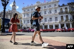 Wisatawan berjalan di sepanjang jalan di Havana, 20 Desember 2023. (YAMIL LAGE / AFP)