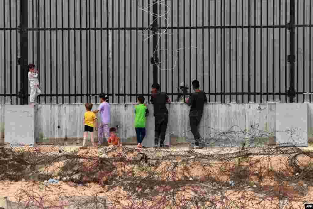 Displaced Palestinian children chat with an Egyptian soldier standing guard behind the fence between Egypt and Rafah in the southern Gaza Strip.