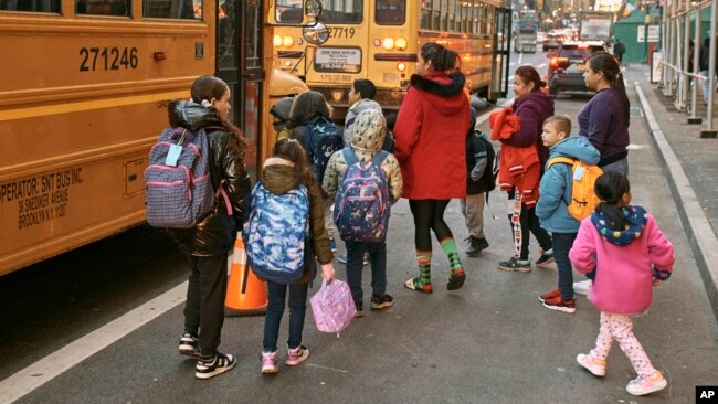 Migrant children prepare to board a school bus while guided by their guardians in front of the Row Hotel that serves as a migrant shelter on Dec. 12, 2023, in New York.