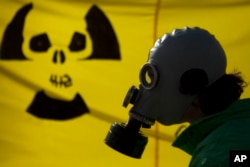 Seorang pria di Berlin mengenakan masker gas memprotes penggunaan pembangkit tenaga nuklir di tengah bencana reaktor nuklir Fukushima di Jepang, 26 Maret 2011. (Foto: Markus Schreiber/AP Photo)