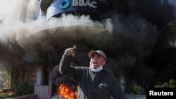 A demonstrator gestures near a bank, set on fire, during a protest against informal restrictions on cash withdrawals and deteriorating economic conditions in Beirut, Lebanon, Feb. 16, 2023.