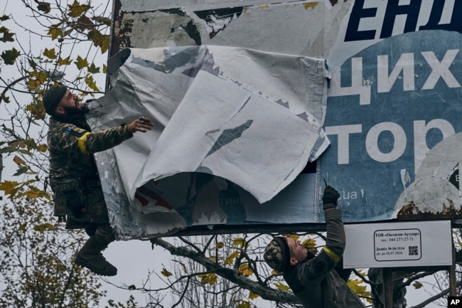 FILE - Ukrainian soldiers remove Russian posters in Kherson, Ukraine, Sunday, Nov. 13, 2022. (AP Photo/LIBKOS)