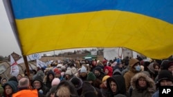 FILE - Ukrainian volunteer Oleksandr Osetynskyi, 44 holds a Ukrainian flag and directs hundreds of refugees after fleeing from the Ukraine after arriving at the border crossing in Medyka, Poland, March 7, 2022.