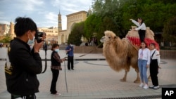 FILE - Tourists pose for photos with a camel outside the Id Kah Mosque in Kashgar in western China's Xinjiang Uyghur Autonomous Region, as seen during a government organized trip for foreign journalists, on April 19, 2021.
