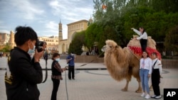 资料照片：2021年4月19日，游客在新疆维吾尔自治区喀什的艾提尕尔清真寺外与骆驼合影。（美联社照片）