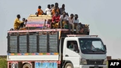 FILE - People ride with furniture and other items atop a truck moving along a road from Khartoum to Wad Madani at the locality of Kamlin, about 80 kilometers southeast of Khartoum, on June 22, 2023.