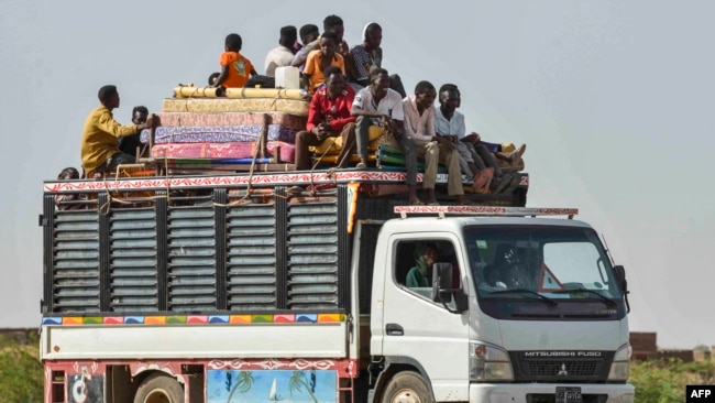 FILE - People ride with furniture and other items atop a truck moving along a road from Khartoum to Wad Madani at the locality of Kamlin, about 80 kilometres southeast of Khartoum, on June 22, 2023.